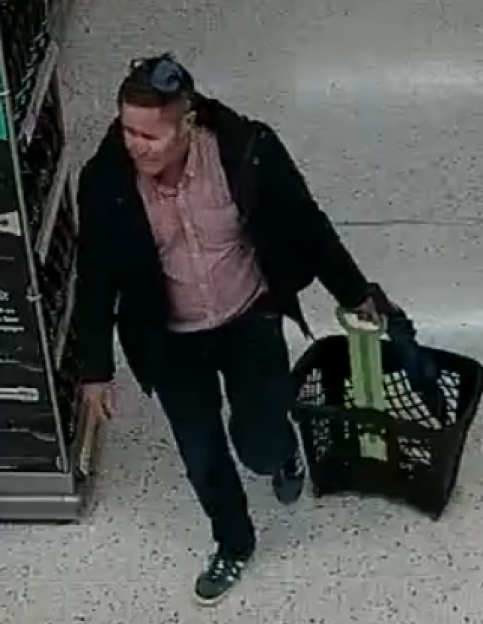 Surveillance image of a man in a dark jacket and pink shirt pushing a shopping basket.