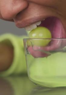 Person dipping a green grape into a glass of water.