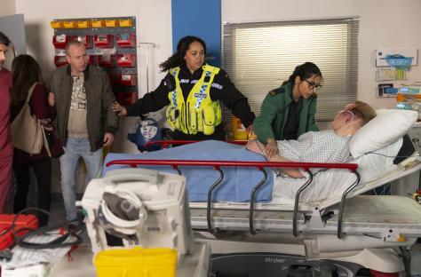 A bloodied man lies on a hospital stretcher surrounded by police and medical personnel.