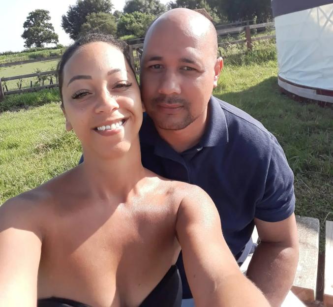 A man and woman posing for a selfie outside with a yurt in the background.