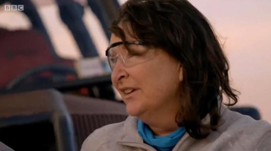 A woman wearing safety glasses speaks emotionally.
