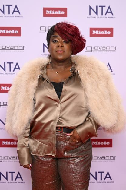 Tameka Empson on the red carpet in a light brown satin shirt, fuzzy light brown coat, and sparkly brown pants.