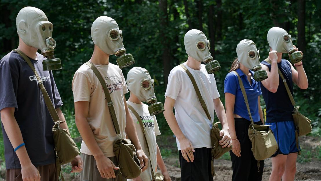 Ukrainian children abducted by Russia, wearing gas masks and carrying shoulder bags, used to make war drones.