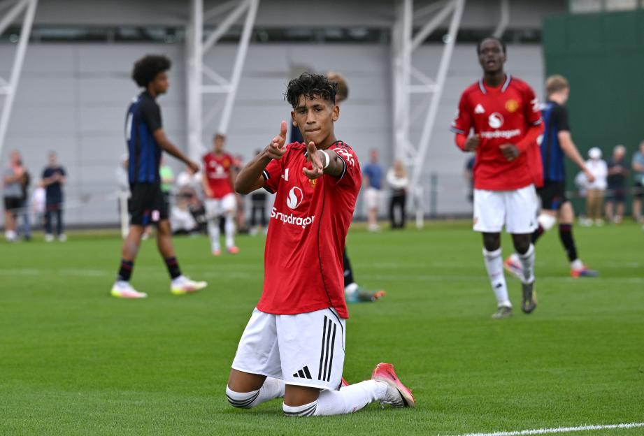 Manchester United's JJ Gabriel kneels on the field celebrating a goal.