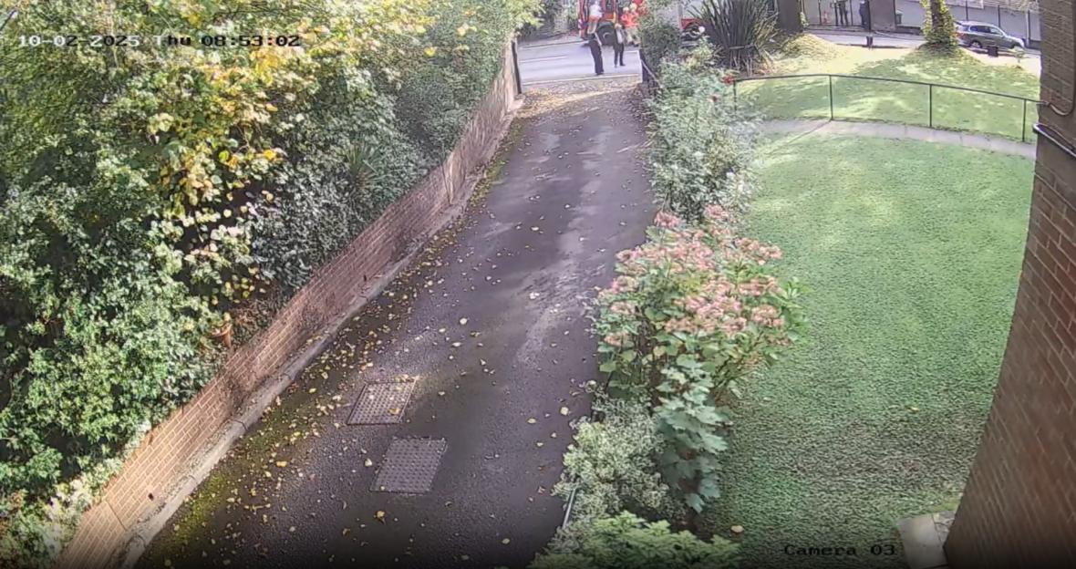 Aerial view of a paved driveway leading to a street with people, a red vehicle, and a grey car.
