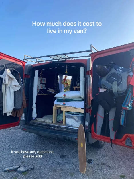 Photo of the inside of a van conversion, showing a bed, clothes, and other items.