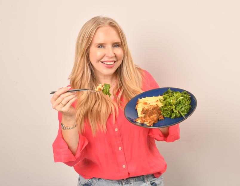 Woman holding a plate of food and eating a forkful.