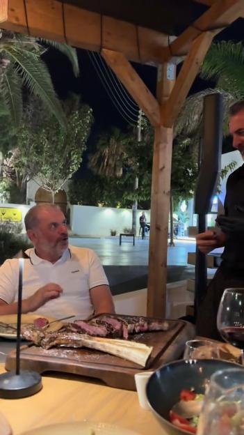 Ange Postecoglou and Stefanos Saratsis sharing a tomahawk steak at an outdoor restaurant.