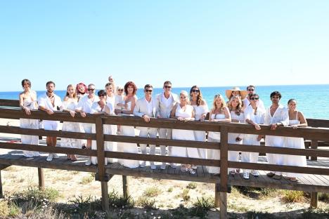 Group of people in white clothing posing on a boardwalk by the ocean.