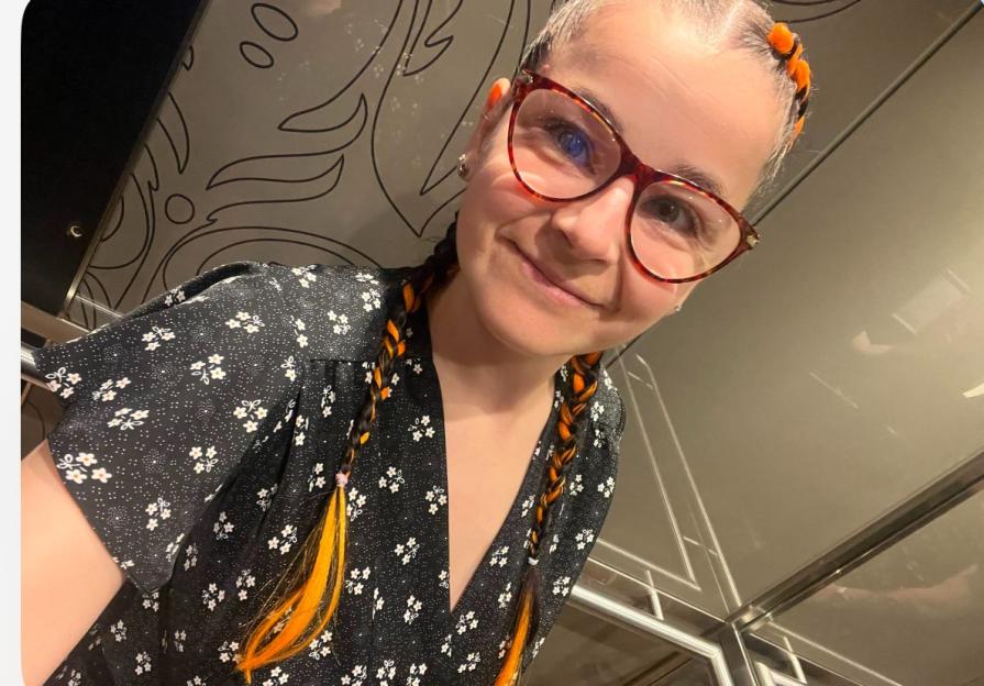 Woman with orange and black braids and glasses in an elevator.