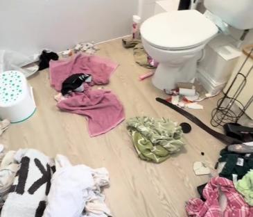 Messy bathroom floor with clothes and towels.