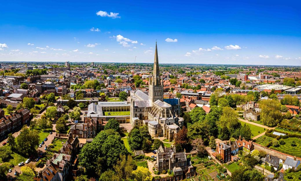 Aerial view of Norwich, England, with Norwich Cathedral at the center surrounded by houses and green trees.