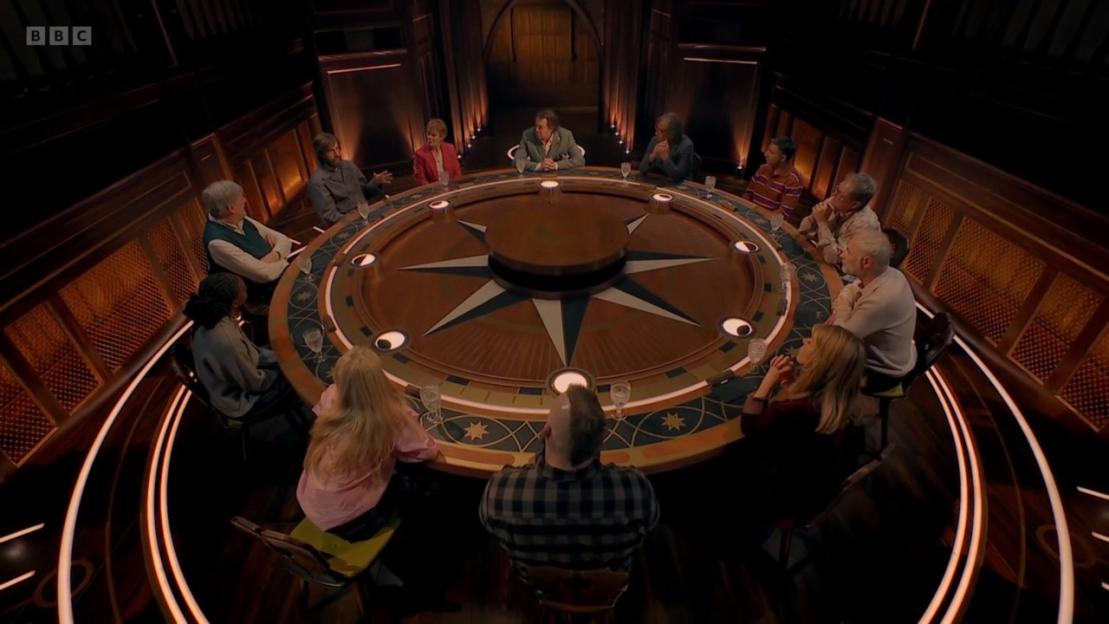 Celebrities Jonathon Ross, Kat Burns, Alan Carr, and Stephen Fry sitting around a large compass-themed table.