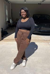 Woman in brown pants and black top standing in front of her garage and Tesla.