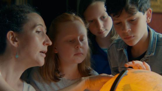 Film still of a woman and three children looking at a globe.