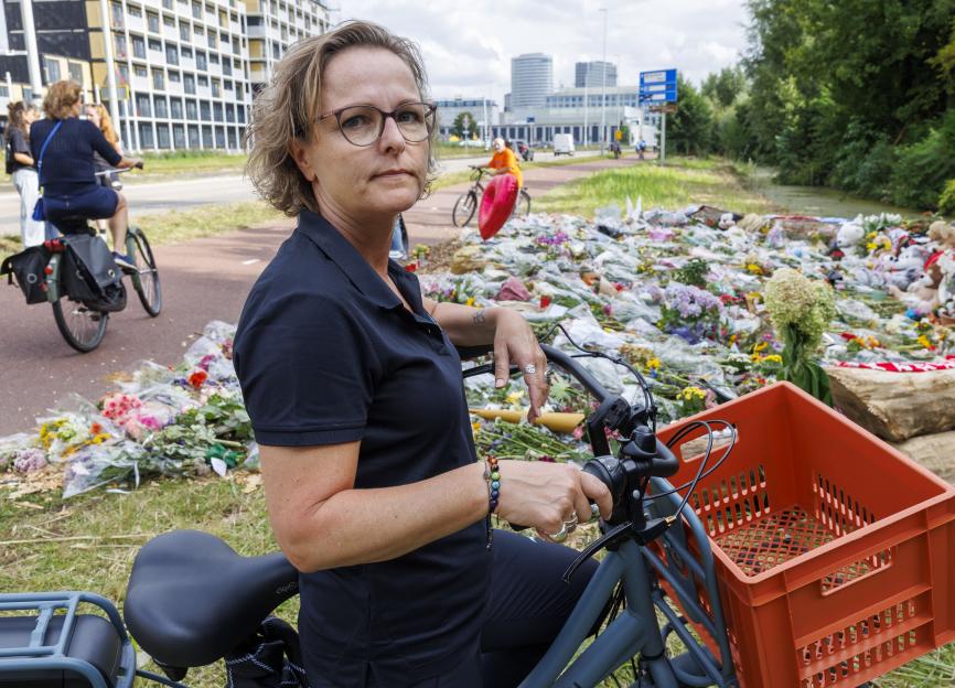 Woman on bicycle at a memorial with flowers and stuffed animals.