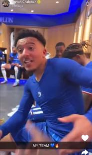 Soccer player in blue uniform with teammates in locker room.