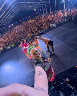 Selfie of a performer on stage with backup dancers and a large audience.