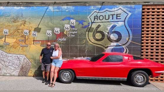 Couple posing with a red car in front of a Route 66 mural.