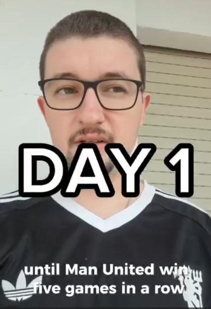 A man with glasses and a goatee, wearing a black shirt, with the words "DAY 1" and "until Man United win five games in a row" superimposed on the image.