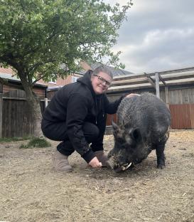 Woman crouching next to her pet pig in a garden.