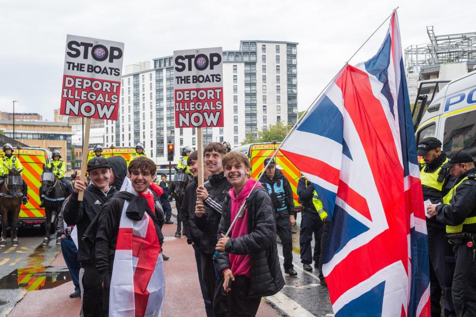 Anti-migrant protesters in Bristol, UK, holding signs and flags.