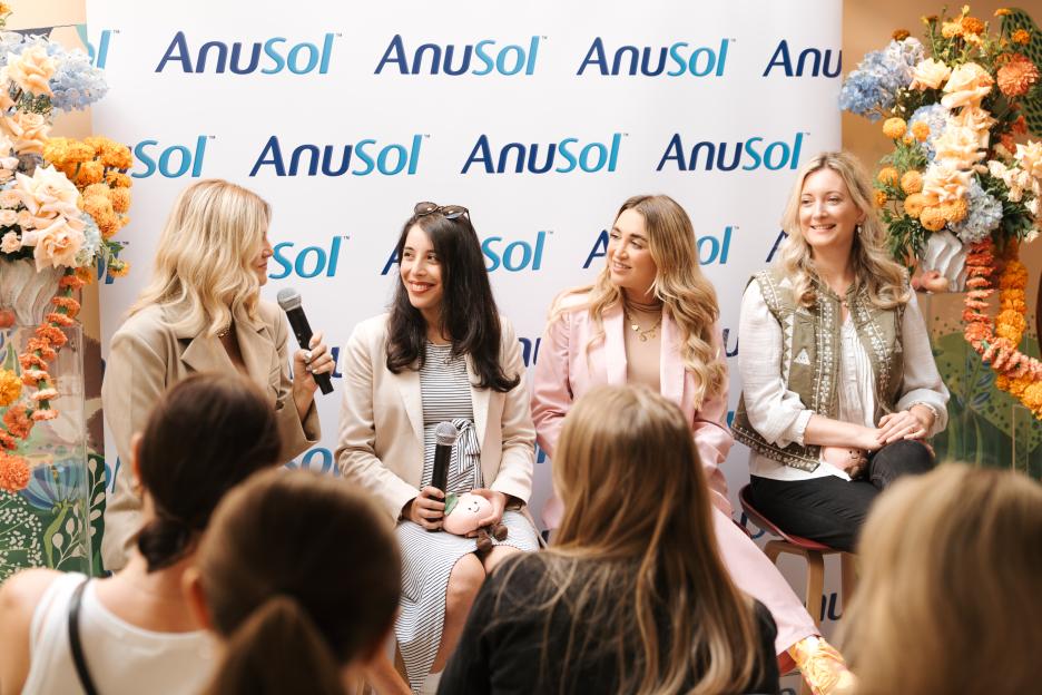Four women sitting on stage speaking to an audience with the Anusol logo behind them.
