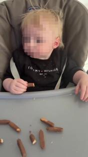 Baby eating sausage rolls in a high chair.