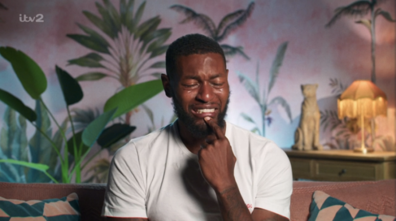 Man crying with his finger near his lips, with a tropical-themed background.
