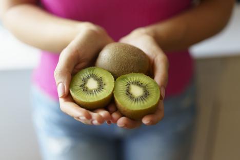 Woman holding two kiwi fruit halves and one whole kiwi.