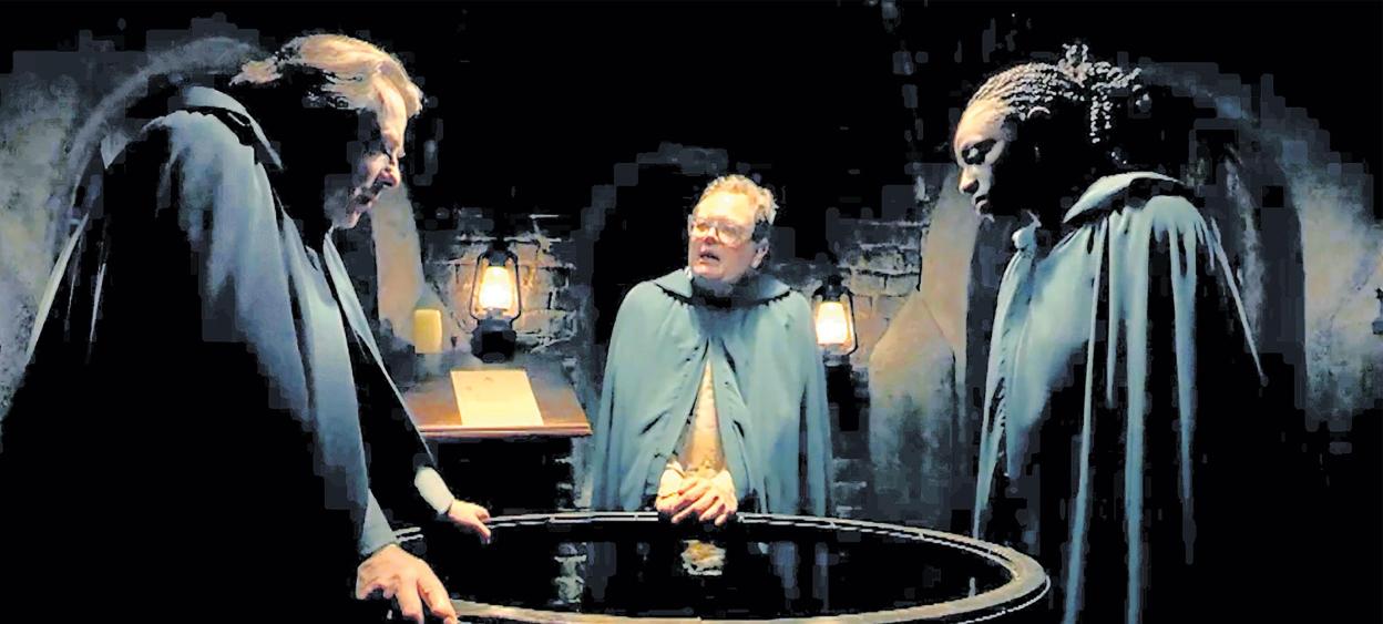 Jonathan Ross, Alan Carr, and Cat Burns in cloaks, gathered around a large basin in a dimly lit room with lanterns.