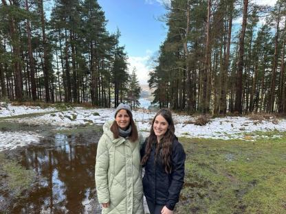 A mother and daughter stand in a snowy forest clearing.