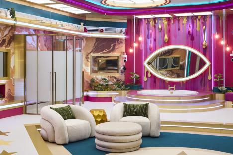 A brightly colored bathroom with a large bathtub, two armchairs, and a large eye-shaped mirror.