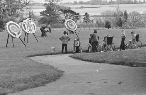 Black and white photo of archery practice at Treloar College, Alton, Hampshire. People in wheelchairs and others participate.