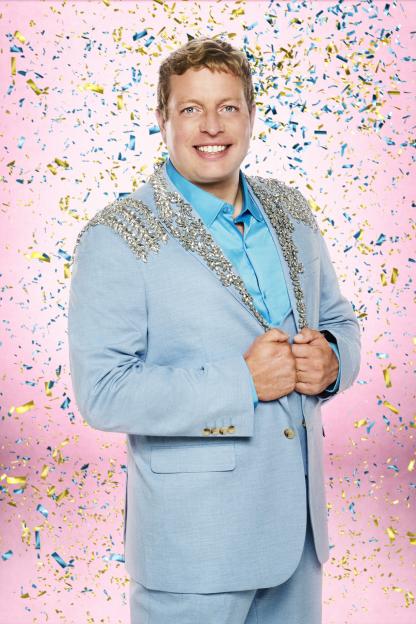 Tom Skinner in a light blue suit with sparkly silver embellishments and a blue shirt, smiling at the camera with confetti falling around him.