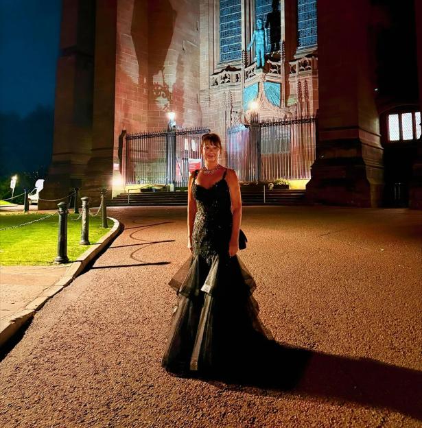 Woman in a black dress in front of a church at night.