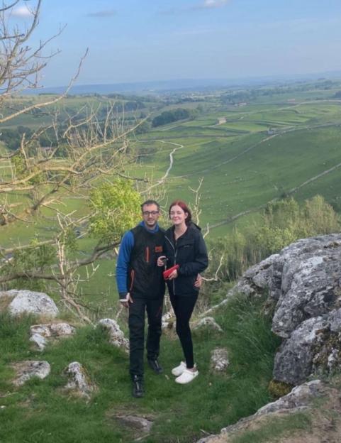 Two individuals posing for a photo on a rocky hill overlooking a vast green valley.