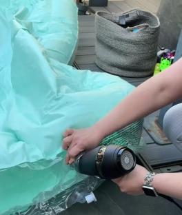 A person inflating a paddling pool using a hairdryer and an empty bottle.