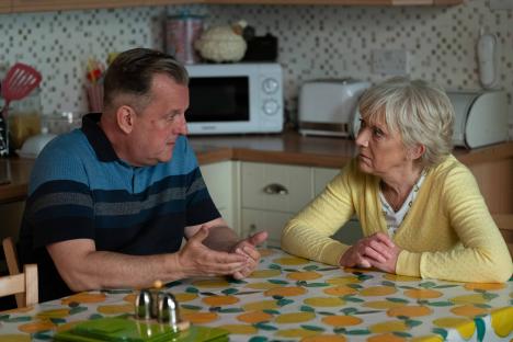 Harvey Monroe and Jean Slater having a conversation at a kitchen table.