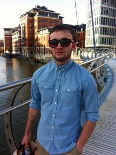 Man in sunglasses and light blue shirt on a bridge.