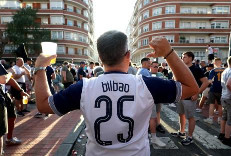 A Bilbao soccer fan with number 25 on his jersey holds a beer and gestures with his other arm.