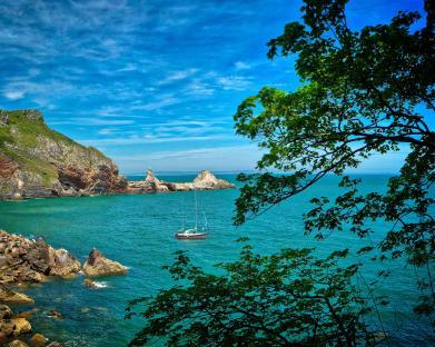 Sailboat in a cove near rocky cliffs.