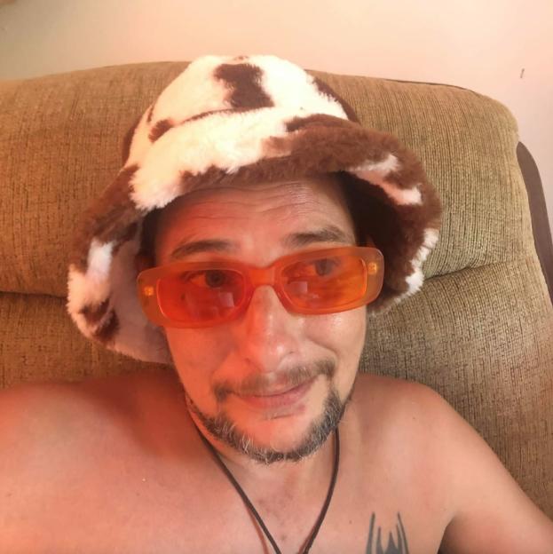 Close-up photo of a man wearing orange sunglasses and a cow-print hat.