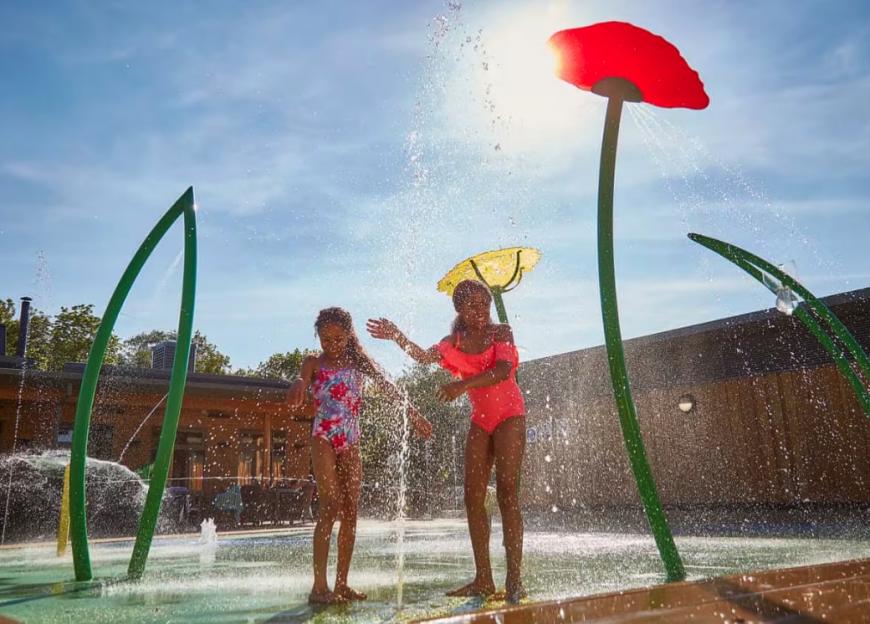 Two girls playing in a water spray park.