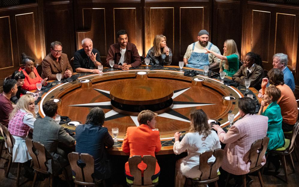 Cast of The Celebrity Traitors seated around a large circular table.