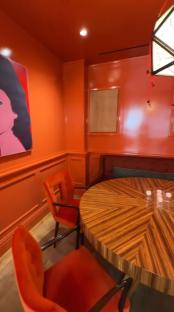 Interior view of a dining area with an orange color scheme, featuring a round wooden table and orange velvet chairs.