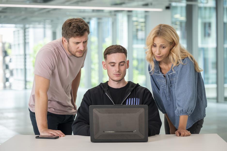 Three people looking at a laptop.