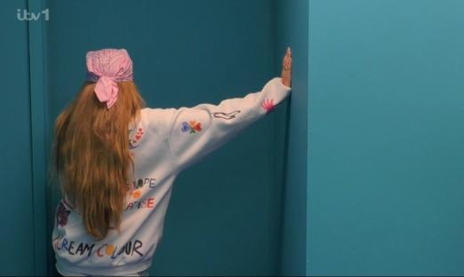 Woman with long hair and a pink bandana leaning against a teal wall.