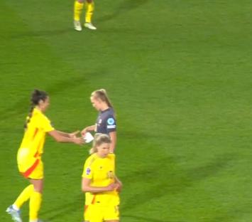 Three female soccer players on a field, two in yellow exchanging something.