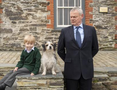 A boy, a dog, and a man in a suit stand outside a stone building.